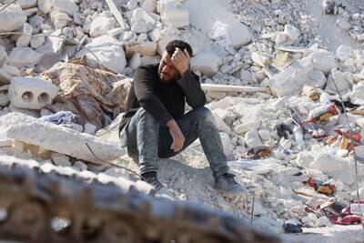 A distraught resident, pictured on February 14, sits on the ruins of the house where relatives had lived. Reuters