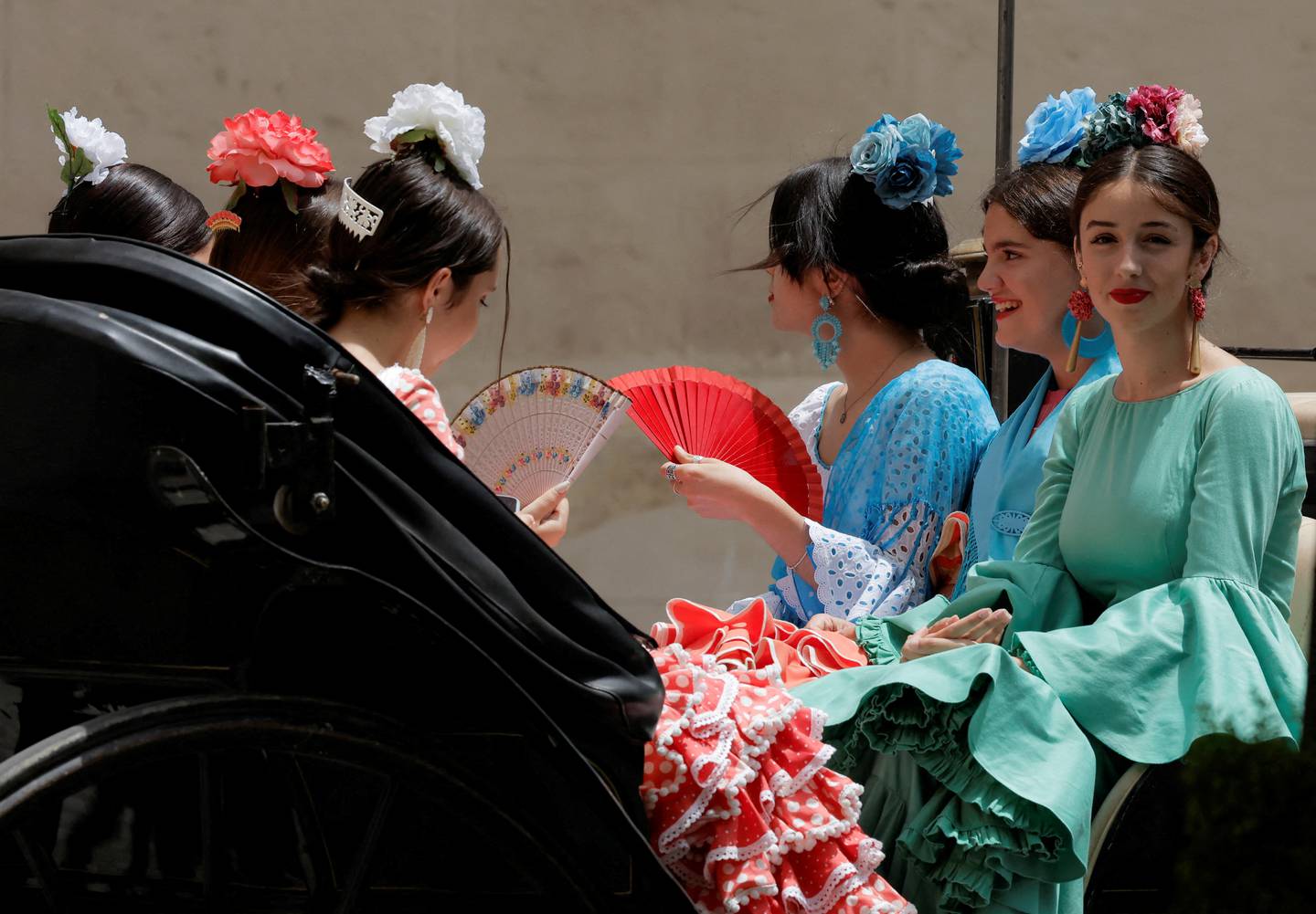 Women wearing traditional sevillana dresses use fans to cool off as they sit on a horse-drawn carriage in Cordoba, Spain, on May 21, 2022.  Reuters