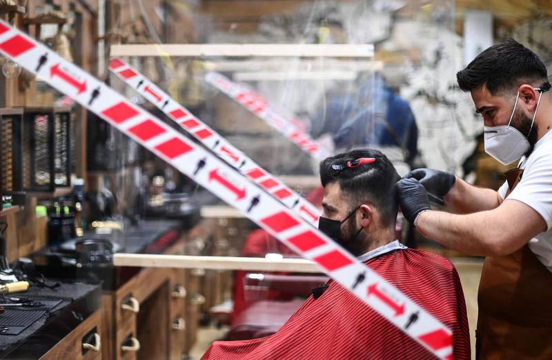 A hairdresser cuts the hair of a client in Dortmund, surrounded by screens and social distance reminders. AFP