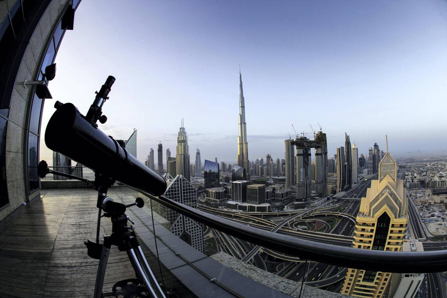 A telescope sits on the outdoor deck of a skyscraper overlooking the city skyline towards the Burj Khalifa tower, center, and the Address Sky View, center right, under construction by developers Emaar Properties PJSC, in Dubai, United Arab Emirates, on Wednesday, April 11, 2018. Transformed into a flamboyant city state from an impoverished Gulf port in less than 50 years, Dubai defied geology to build skyscrapers and elaborately shaped islands in the sea. Photographer: Christopher Pike/Bloomberg