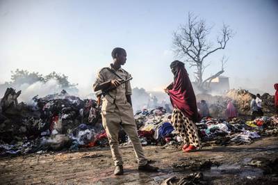 A woman and a police walk by piles of cloths remaining after a fire broke overnight in Mogadishu's biggest market, the Bakara Market. AFP
