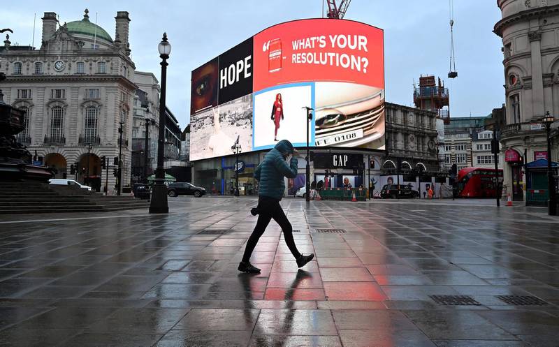 A pedestrian shelters from the rain as they walk across an almost deserted Piccadilly Circus in London as Britain enters a national lockdown. AFP