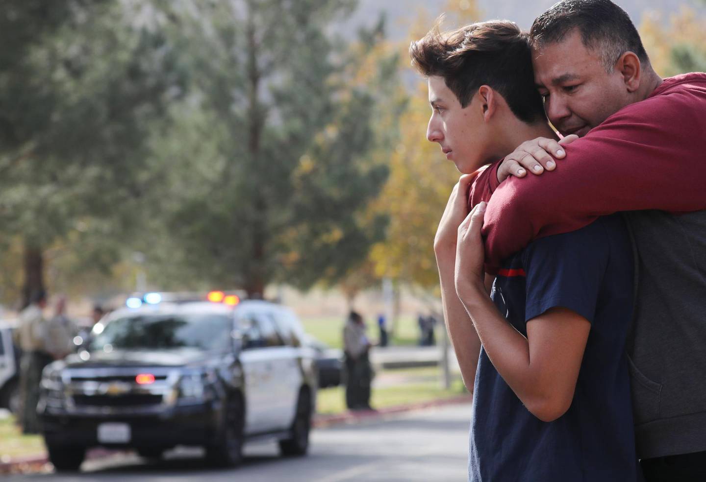 TOPSHOT - SANTA CLARITA, CALIFORNIA - NOVEMBER 14: Marco Reynoso (R) hugs his son, 11th-grader Dylan Reynoso, after reuniting at a park near Saugus High School after a shooting at the school left two students dead and three wounded on November 14, 2019 in Santa Clarita, California. A suspect in the shooting is being treated at a local hospital for a gunshot wound to the head.   Mario Tama/Getty Images/AFP / AFP / GETTY IMAGES NORTH AMERICA / MARIO TAMA
