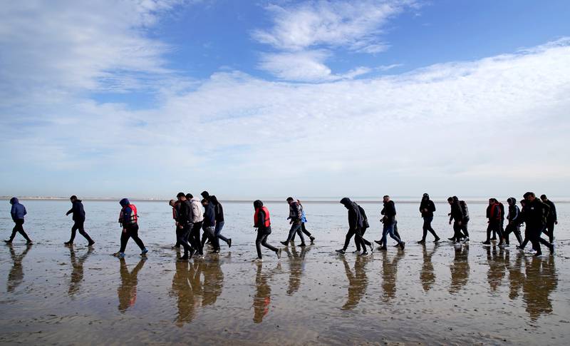 A group of people thought to be migrants walk along the beach after being brought to Dungeness in Kent on a RNLI Lifeboat. PA
