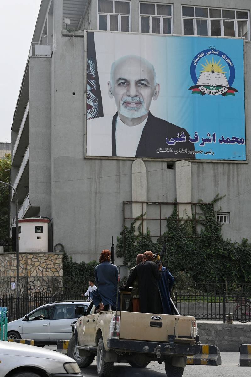 Taliban fighters pass a poster of Afghan President Ashraf Ghani in Kabul. AFP