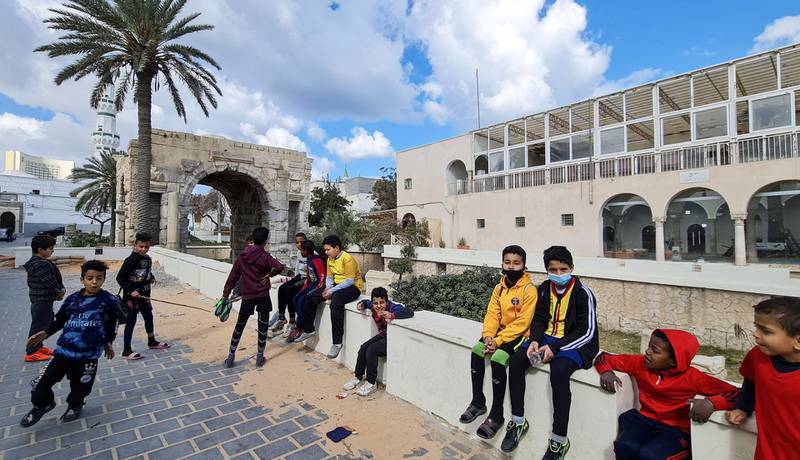 Children sit in a square with the Roman Arch of Marcus Aurelius in the background, in Tripoli's Old City. AFP