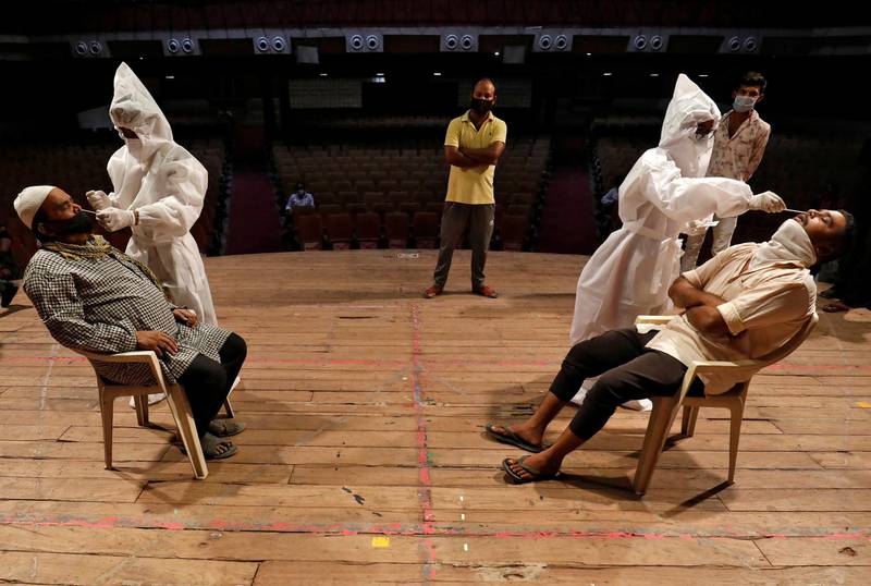 Healthcare workers in personal protective equipment collect swab samples from men during a rapid antigen testing campaign for the coronavirus at an auditorium turned into a testing centre in Ahmedabad, India. Reuters