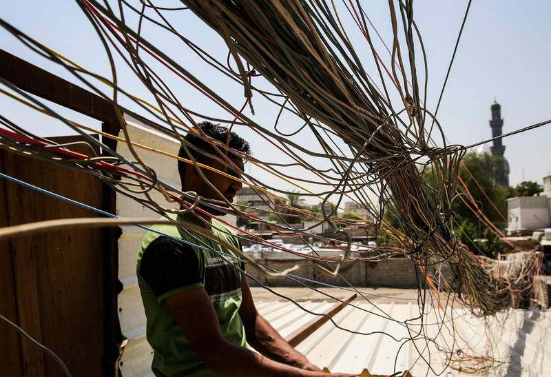 (FILES) In this file photo taken on July 29, 2018, a man checks the wiring on electric cables reaching out to homes in Saadoun Street in the Iraqi capital Baghdad, as chronic power shortages have forced residents to buy electricity from private entrepreneurs who run generators on street corners across the country. With a freshman at the helm, Iraq's electricity ministry is planning a long-awaited overhaul of the broken sector to both meet US pressure to halt Iranian power imports and head off summertime protests over chronic cuts. Baghdad hopes it will generate enough megawatts to feed demand by summer, when cuts can leave millions powerless for up to 20 hours per day. / AFP / SABAH ARAR
