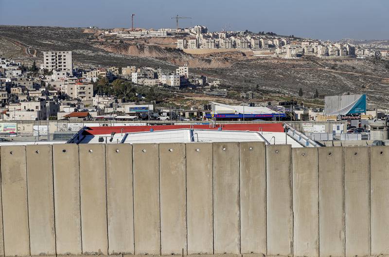 This picture taken on February 13, 2020 shows a section of Israel's separation barrier on the outskirts of Israeli-annexed East Jerusalem in the foreground, the Qalandia camp for Palestinian refugees in the occupied West Bank behind, and Israeli construction cranes at work on new housing units in the Jewish settlement of Kochav Ya'akov in the background.