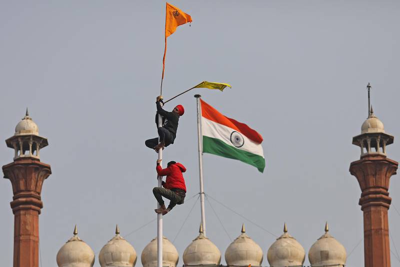 Farmers ascend a flag pole while protesting at the Red Fort during a tractor rally in New Delhi, India. Bloomberg