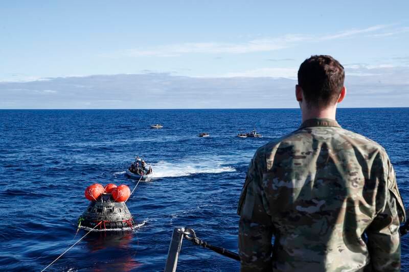 A member of the Air Force watches as the Orion capsule is towed towards the USS Portland. EPA