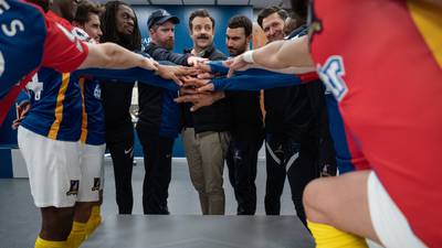 This image released by Apple TV shows Jason Sudeikis, center, Brendan Hunt, center left, and Brett Goldstein, center right, with cast members in a scene from the season three finale of "Ted Lasso. " (Colin Hutton / Apple TV via AP)