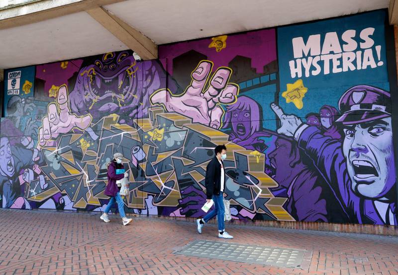 Pedestrians, wearing protective masks, walk past a street art mural, depicting "Mass Hysteria" related to the Covid-19 pandemic, in Birmingham, U.K. Bloomberg
