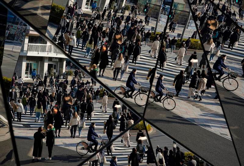 Passersby wearing protective face masks are reflected in mirrors at the Omotesando fashion district in Tokyo. EPA