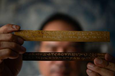 This photo taken on June 11, 2019 shows cultural advocate Leo Emmanuel Castro holding pieces of bamboo inscribed with indigenous Baybayin script at his shop in Manila.