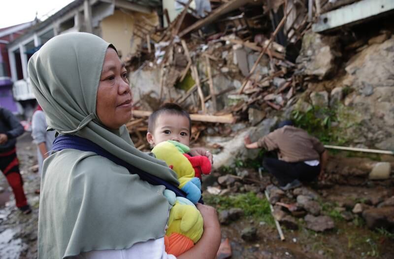 A mother holds her son in front of her damaged house in Cianjur after the 5.6 magnitude earthquake. EPA