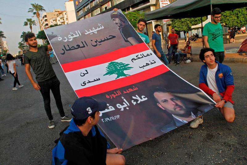 Lebanese demonstrators carry a poster bearing the portraits of Alaa Abou Fakhr, who was shot dead south of Beirut the day before, and Hussein Atar, a demonstrator who was killed during a protest last month, during a gathering in the southern city of Sidon (Saida) on November 13, 2019, nearly a month into an unprecedented anti-graft street movement. Street protests erupted, the night before, after President Michel Aoun defended the role of his allies, the Shiite movement Hezbollah, in Lebanon's government. Protesters responded by cutting off several major roads in and around Beirut, the northern city of Tripoli and the eastern region of Bekaa. / AFP / Mahmoud ZAYYAT

