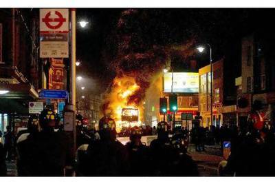 A double decker bus burns as riot police try to contain a large group of people on a main road in Tottenham, north London on August 6 2011. Two police cars were on Saturday set ablaze in north London following a protest over the fatal shooting of a 29-year-old man in an armed stand-off with officers. The patrol cars were torched as dozens gathered outside the police station on the High Road in Tottenham.