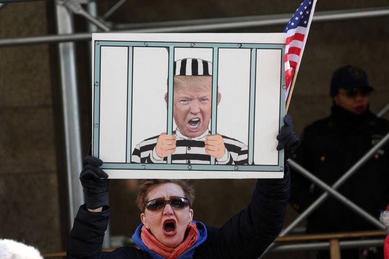 A demonstrator holds a sign depicting Mr Trump behind bars. Getty 