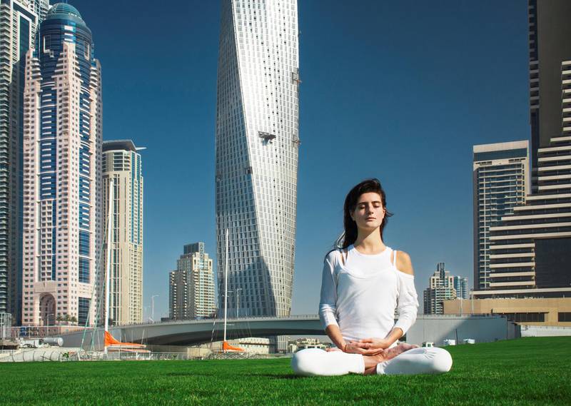 Yoga and meditation in a modern urbanistic city. Young attractive girl - yoga meditates against huge modern skyscrapers of Dubai. The Area of Dubai Marina perfectly combines huge buildings and vacation spots of inhabitants of the area. Grain added