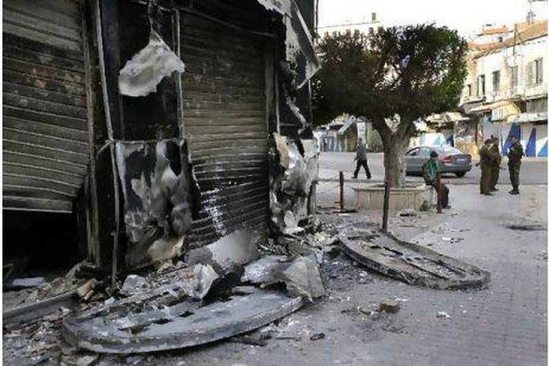 Syrian soldiers, right, patrol near a shop burned in Sunday's clashes between protesters and security forces in Latakia.