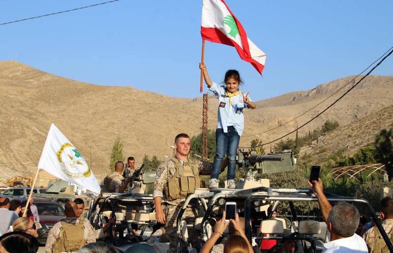 A girl scout waves a national flag next to a Lebanese Army soldier on a military vehicle, during a celebration of the soldiers' return from battling Islamic State (IS) group jihadists on the country's eastern front bordering with Syria, in the eastern town of Ras Baalbek on August 30, 2017. / AFP PHOTO / STRINGER