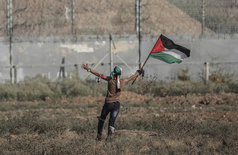 epa07788799 A Palestinian protester waves a Palestinian flag next to Israeli troops near the border between Israel and eastern Gaza Strip, 23 August 2019.  EPA/MOHAMMED SABER