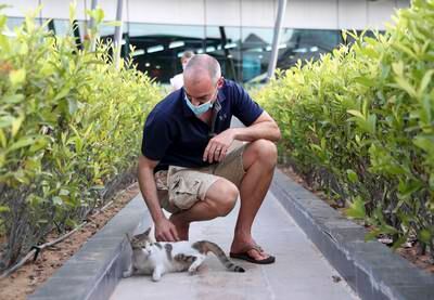 Sean Steyn, a resident of Al Bandar, plays with Honey, a stray cat that lives on the site of the development at Al Raha Beach. Khushnum Bhandari /  The National