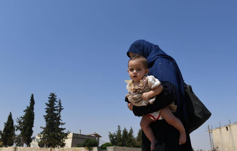 A Syrian woman holds her child walks at the Abu Duhur crossing on the eastern edge of Idlib province on August 20, 2018. - Civilians are coming from rebel-held areas in Idlib province and entering regime-held territories through the Abu Duhur crossing, some of them returning to their villages that were recaptured by the regime forces earlier this year. (Photo by George OURFALIAN / AFP)