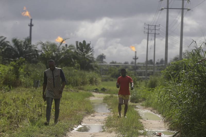 Two men walk past gas flares belonging to the Agip Oil company in Idu, in the Niger Delta area of Nigeria. AP