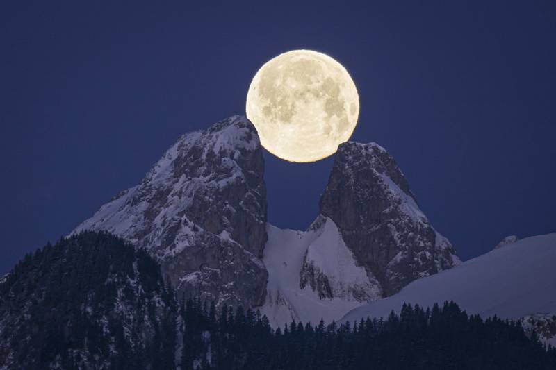 The full moon looks like its being held up by the twin peaks of Les Jumelles, near Aigle, Switzerland. AP