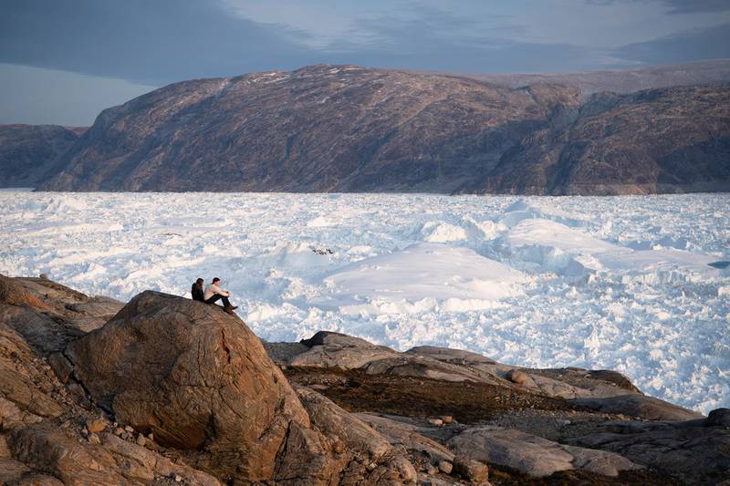 NYU student researchers sit on top of a rock overlooking the Helheim glacier.