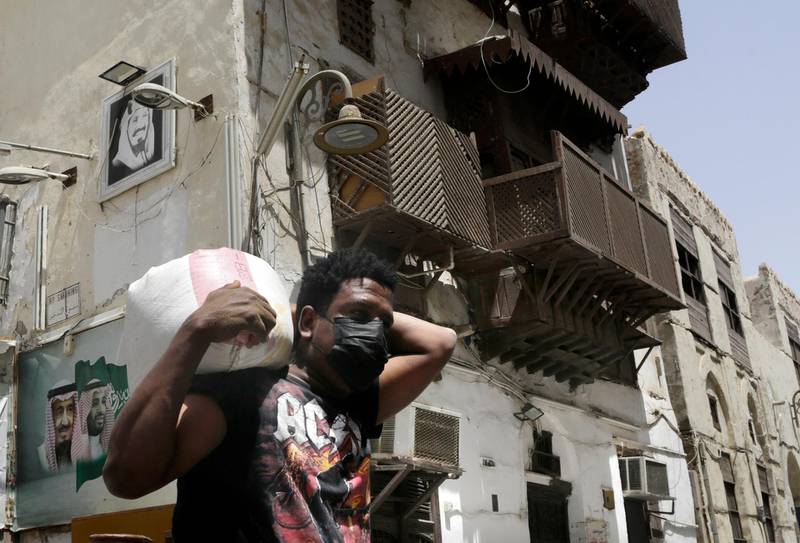 A worker, wearing a face mask as a precaution against the coronavirus, carries a load at Jiddah's historical district. AP