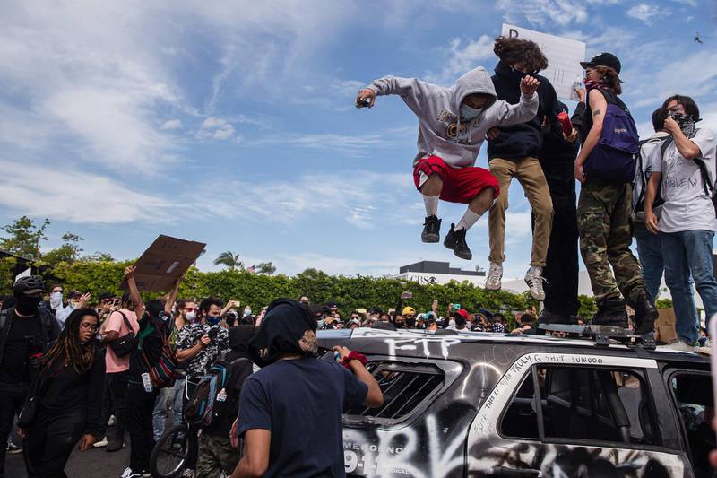 Demonstrators jump on a damaged police vehicle in Los Angeles on May 30, 2020 during a protest against the death of George Floyd, an unarmed black man who died while while being arrested and pinned to the ground by the knee of a Minneapolis police officer. Clashes broke out and major cities imposed curfews as America began another night of unrest Saturday with angry demonstrators ignoring warnings from President Donald Trump that his government would stop violent protests over police brutality "cold." / AFP / ARIANA DREHSLER
