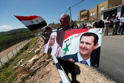 A demonstrator holds portraits of Syrian President Bashar Al Assad next to the ceasefire line between Israel and Syria. EPA