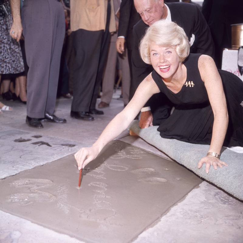 19th January 1961:  American singer and actress Doris Day smiling as she signs her name in cement by her handprints, in front of Mann's (formerly Grauman's) Chinese Theater, on Hollywood Boulevard, Hollywood, California.  (Photo by Hulton Archive/Getty Images)