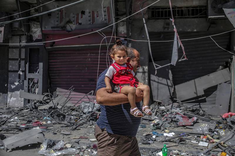 A Palestinian man carries his daughter next to a destroyed tower, following Israeli air strikes in Gaza city. EPA