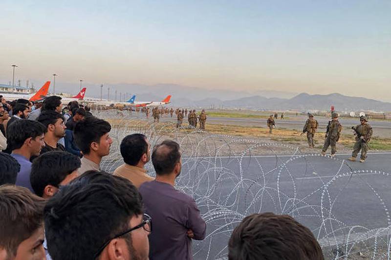 Afghans gather by the runway in Kabul as US soldiers stand guard.