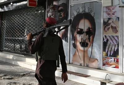 A Taliban fighter walks past a beauty salon with images of women defaced using spray paint in Shar-e-Naw in Kabul on August 18, 2021. AFP