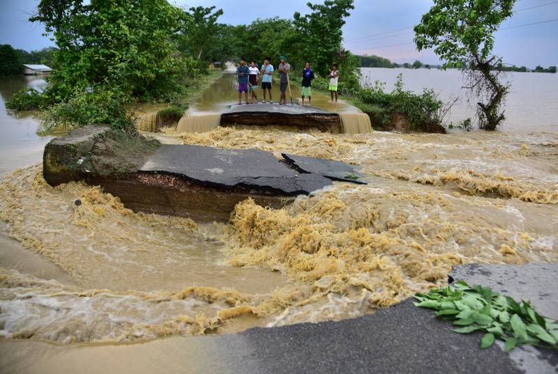 People stand on higher ground on a road damaged by the floodwater after heavy rain in Nagaon district, in the north-eastern state of Assam, India. Reuters