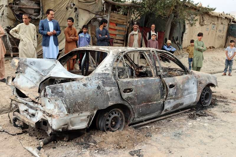 People stand by the shell of a vehicle damaged by a rocket attack. AP