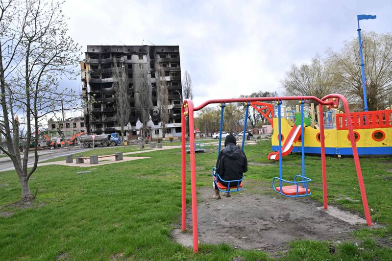 A teenager sits on a playground swing, opposite a gutted apartment block in Borodianka, in the Kyiv region. AFP