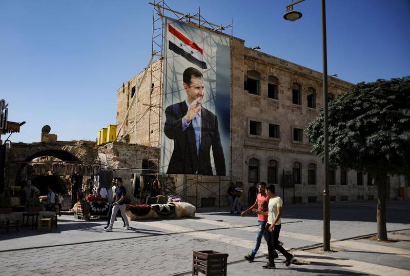 (FILES) In this file photo taken on September 27, 2019 during a guided tour with the Russian army shows men walking past a poster of Syrian President Bashar al-Assad in the old city of Aleppo. Syria is to hold a presidential election on May 26, the parliament speaker announced today, the country's second in the shadow of civil war, seen as likely to keep President Bashar Al-Assad in power. / AFP / Maxime POPOV
