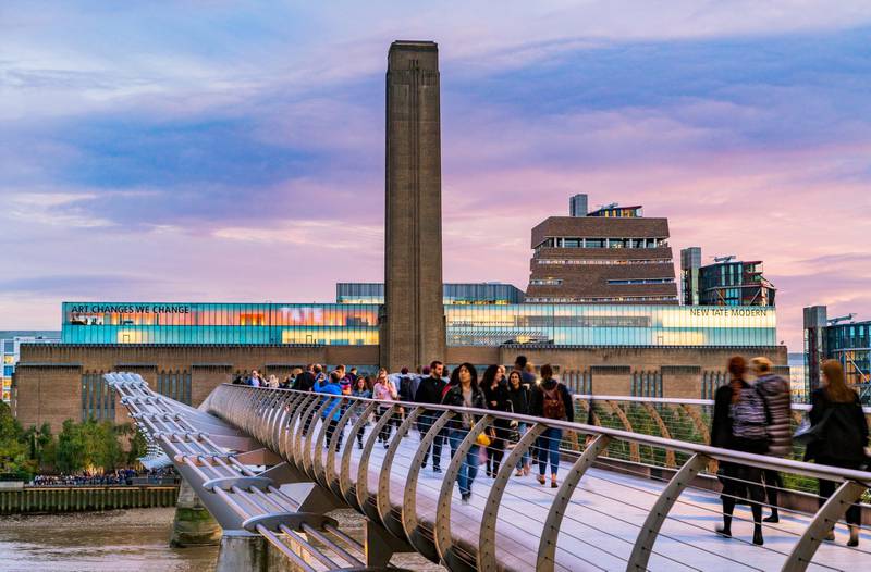 The Tate Modern is seen with tourists crossing the Millennium Bridge in the foreground. Photos.London