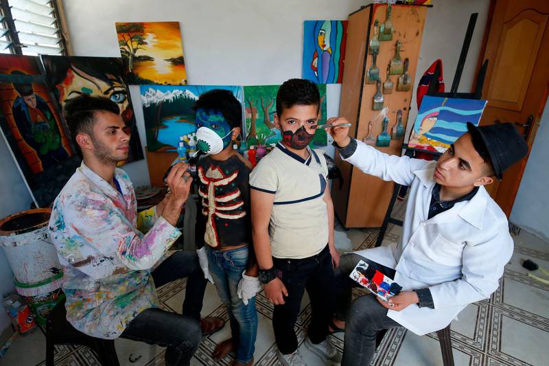 Palestinian artists Hammam Mosallam (L) and Yussef Abu Zerr (R) apply facepaint on a mask and a child's face at their home workshop in the Nusseirat refugee camp in the central Gaza Strip.   AFP