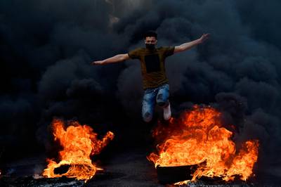 A protester leaps over burning tyres, during a protest against power cuts in Beirut, Lebanon. EPA