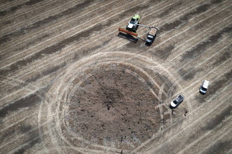 Harvesting in Dnipropetrovsk, with a crater left by a Russian rocket in the foreground. AP
