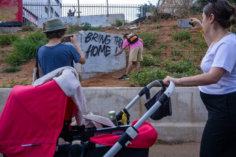 A man writes "bring them home now" with spray paint while families of hostages and their supporters march along the Ayalon highway during the five-day “March for the Hostages.” Getty Images