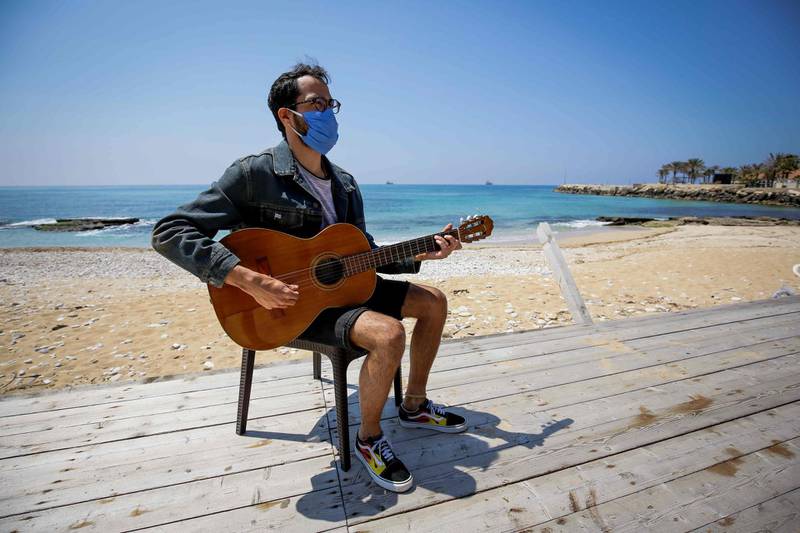Uruguayan singer Walter Javier Maulelo, stuck in Lebanon, plays guitar while wearing a mask alone on a seafront boardwalk in the northern coastal city of Batroun.  AFP