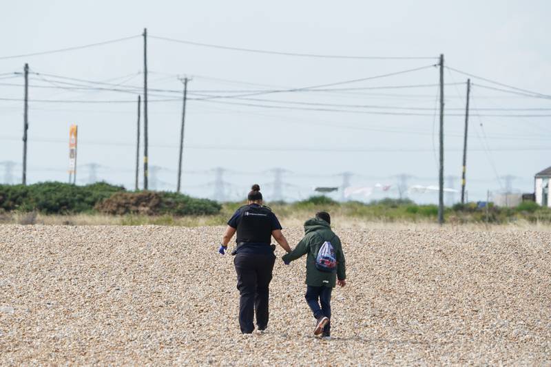 An officer from Immigration Enforcement escorts a child along the beach in Dungeness. PA